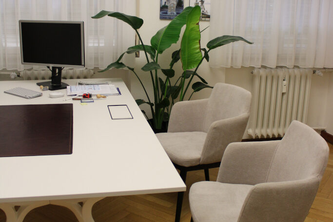 Bürotisch mit zwei Stühlen und einem Computer in einem hellen Raum.