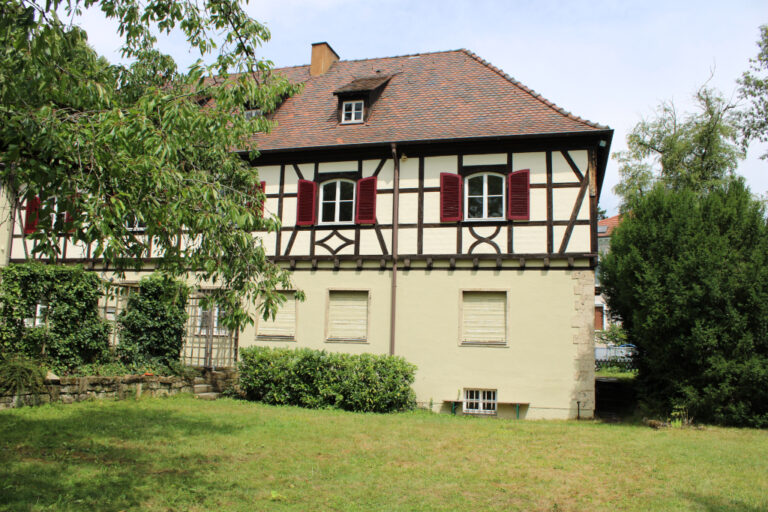 Fachwerkhaus mit roten Fensterläden und grünem Garten im Vordergrund.